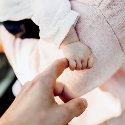 Baby som håller i en vuxens finger - om ICA Försäkrings barnförsäkring