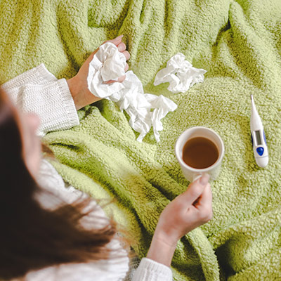 Sjuk kvinna i sängen med te och näsdukar